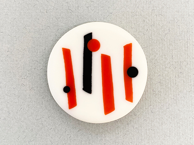 a white circular brooch with abstract red and black lines inside