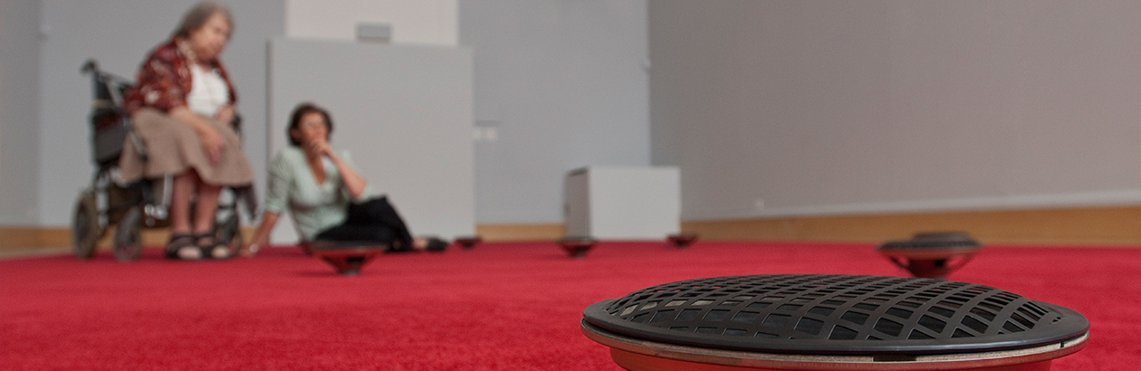 a speaker on a floor covered with red carpet as part of the Prayer installation in the Djanogly Gallery, 2010, with two visitors blurry in the background