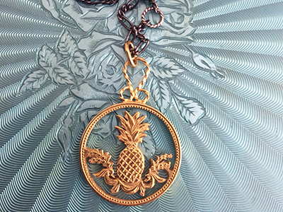 A golden medallion necklace with a pineapple in the centre