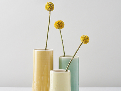 Image of three vases of turquoise, pale yellow, and white, containing a single yellow flower each