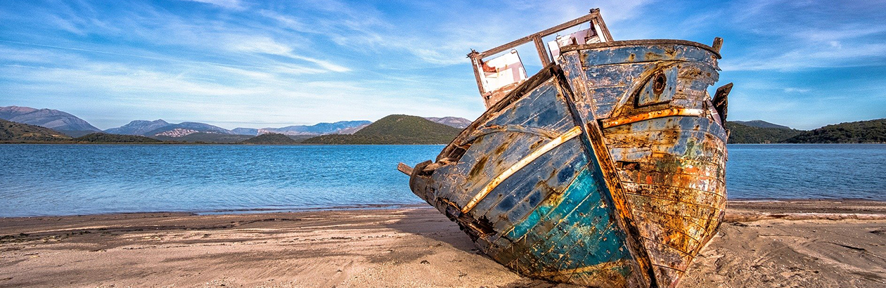Photograph of ship washed up on sands with mountains and sea in the background