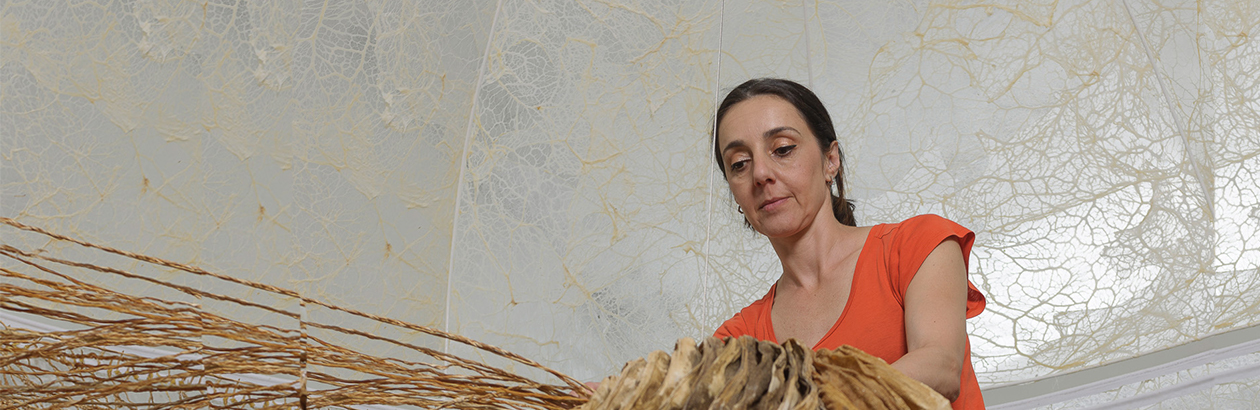 Photograph of Elpida Hadzi-Vasileva on a ladder looking over a brown knotted artwork 